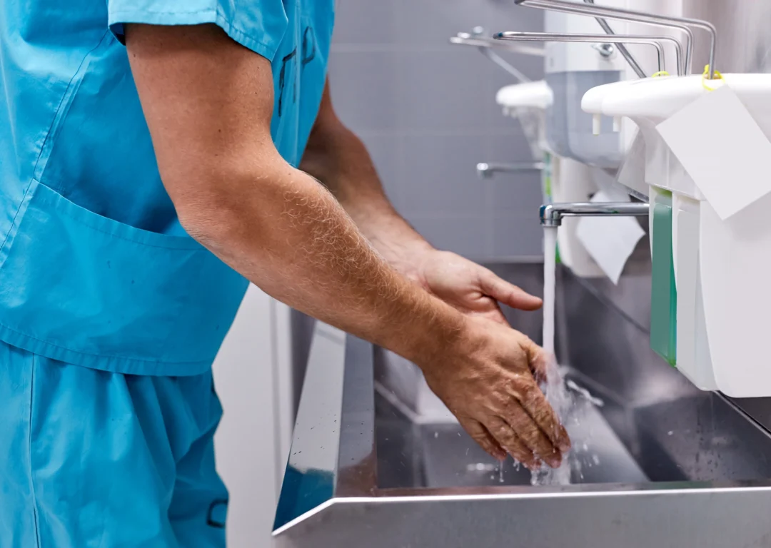 Healthcare professional in scrubs washing hands at metal sink before going into operating theatre.