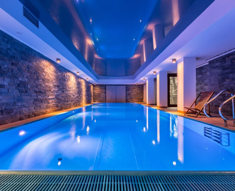 A modern indoor swimming pool, brightly lit with blue underwater lights.