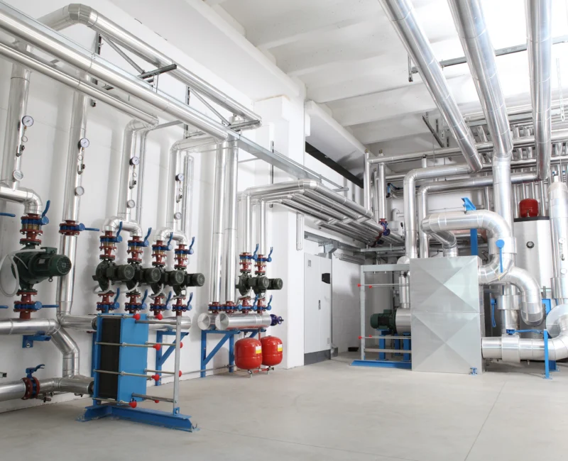 A newly installed plant room with extensive silver insulated pipes, blue and red valves, and pumps.
